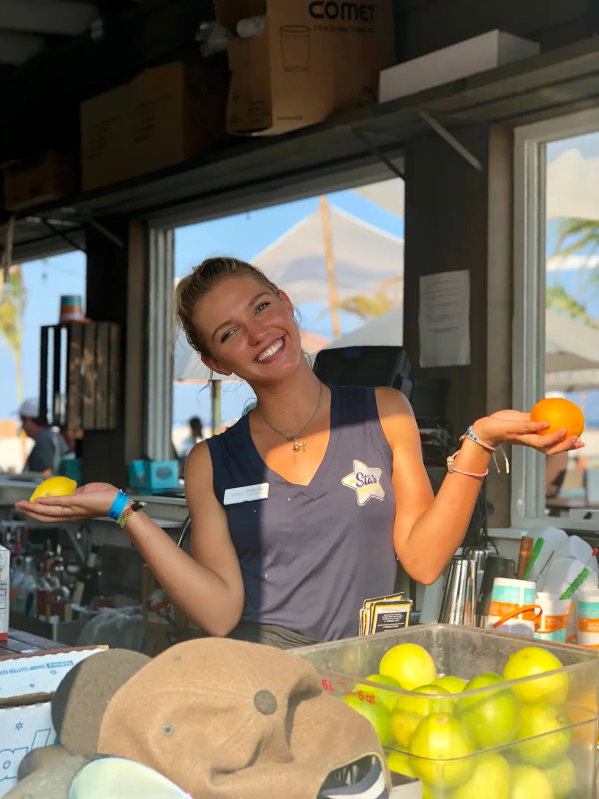 blonde female bartender smiling holding an orange and a lemon behind the bar